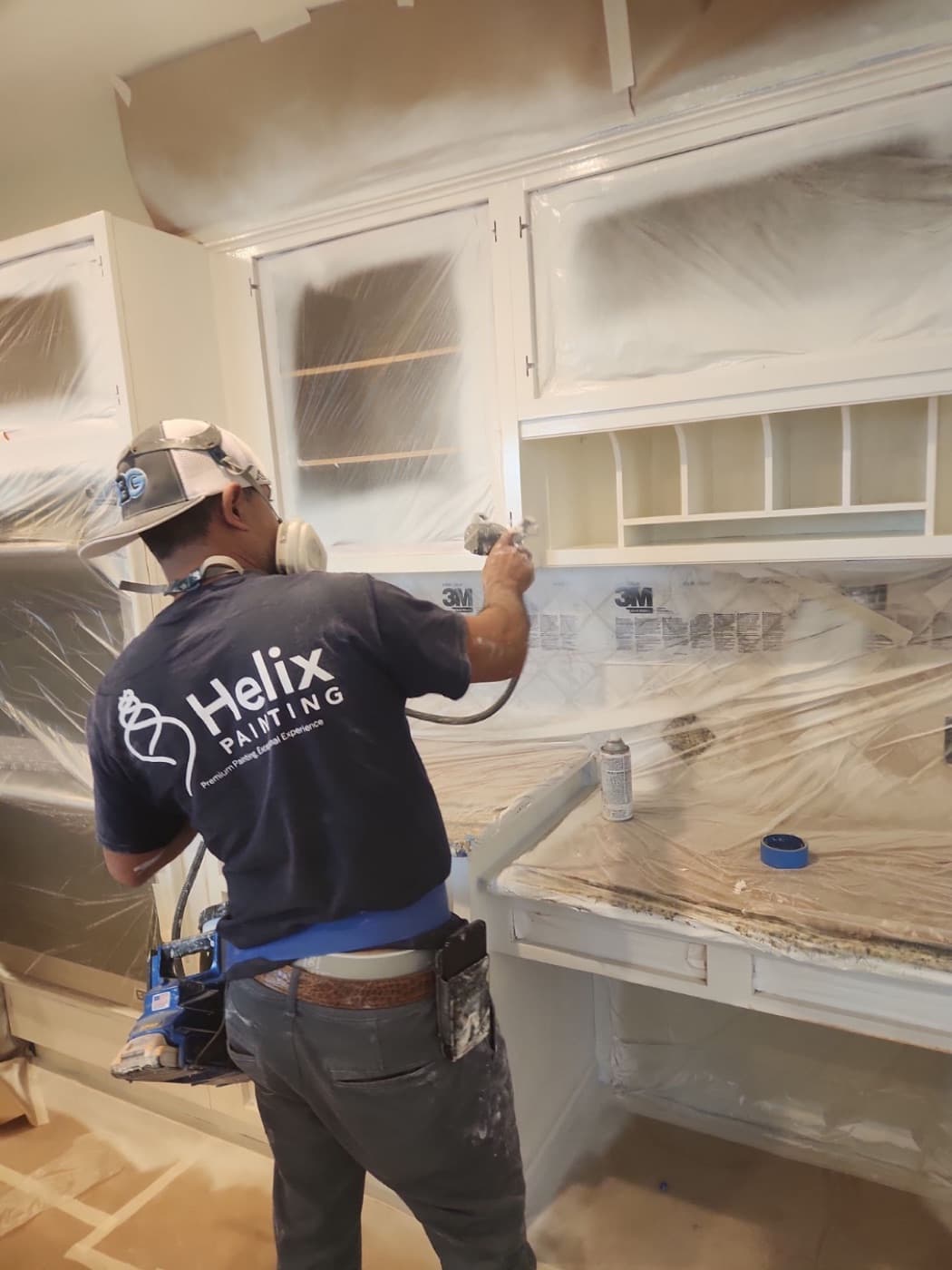 Helix painter in a branded shirt spraying masked kitchen cabinets