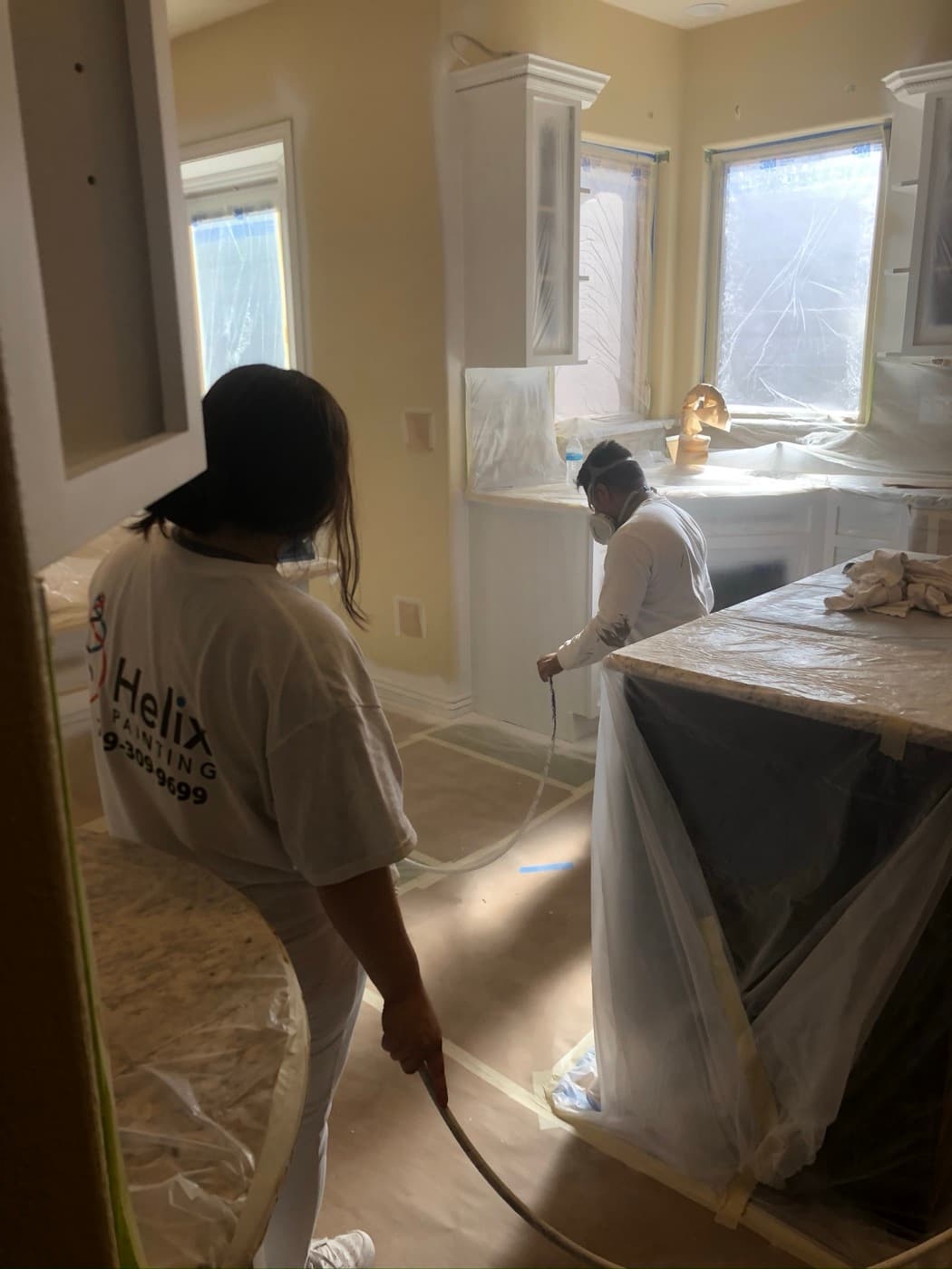 Two Helix painters running a spray line through a masked kitchen