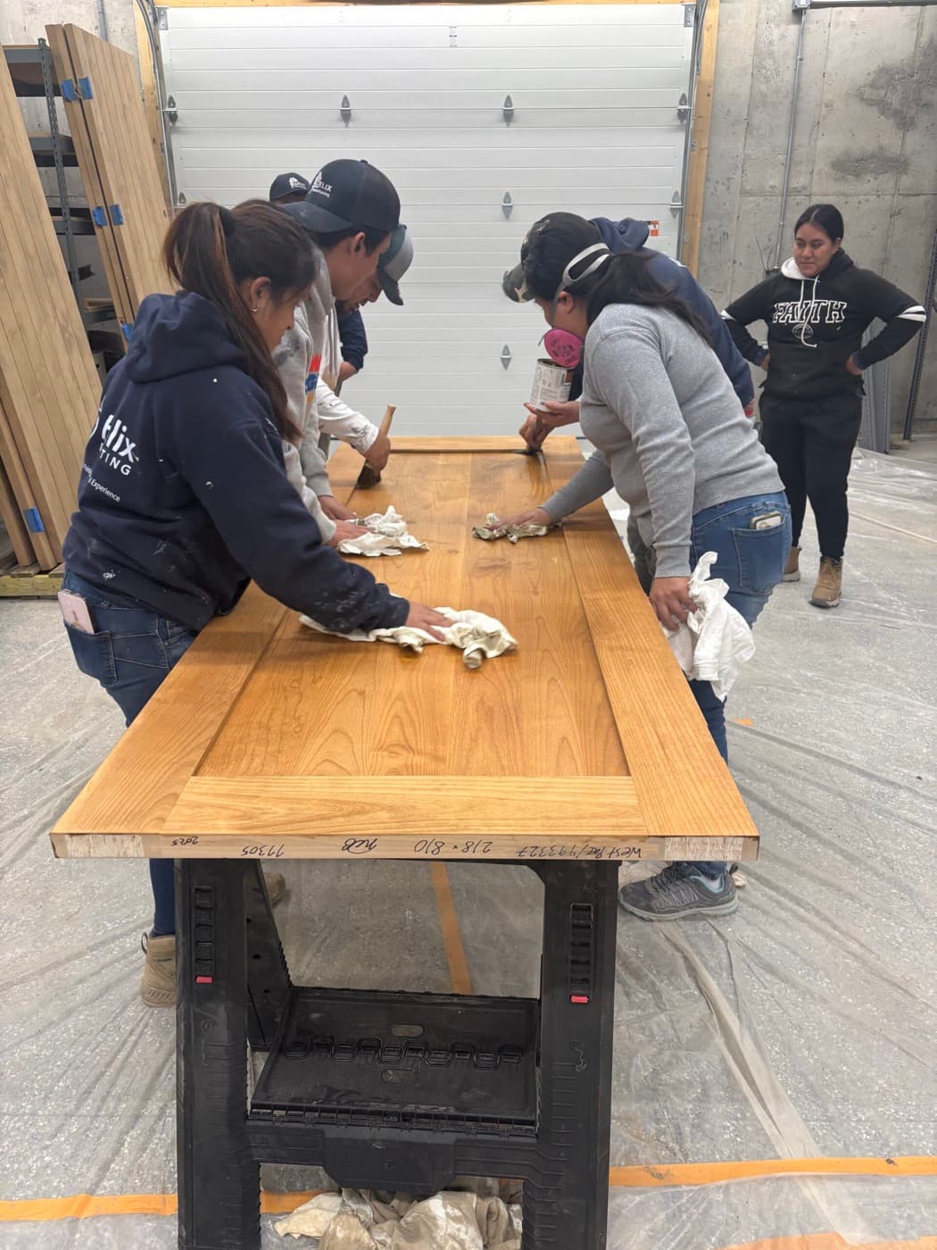 Crew hand-staining a solid timber door laid flat in the shop