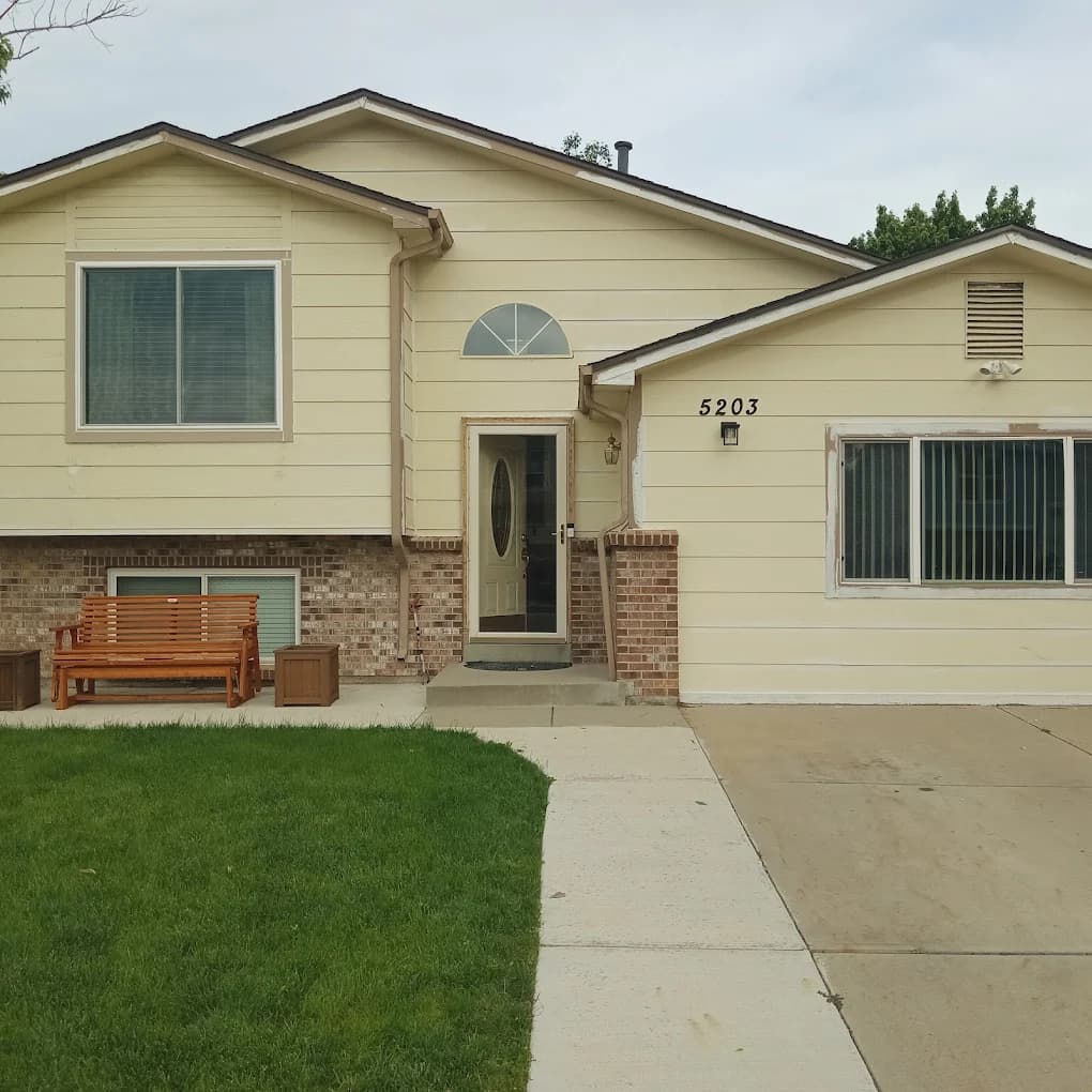 Tan split-level home with white trim and a bench by the door