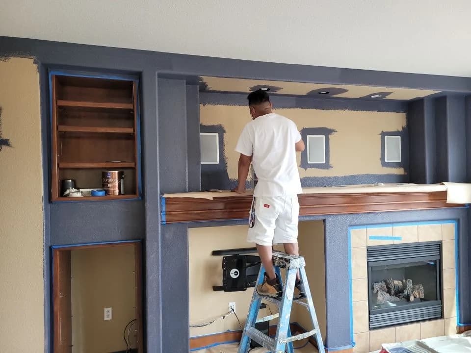 Painter on a ladder finishing a built-in fireplace wall