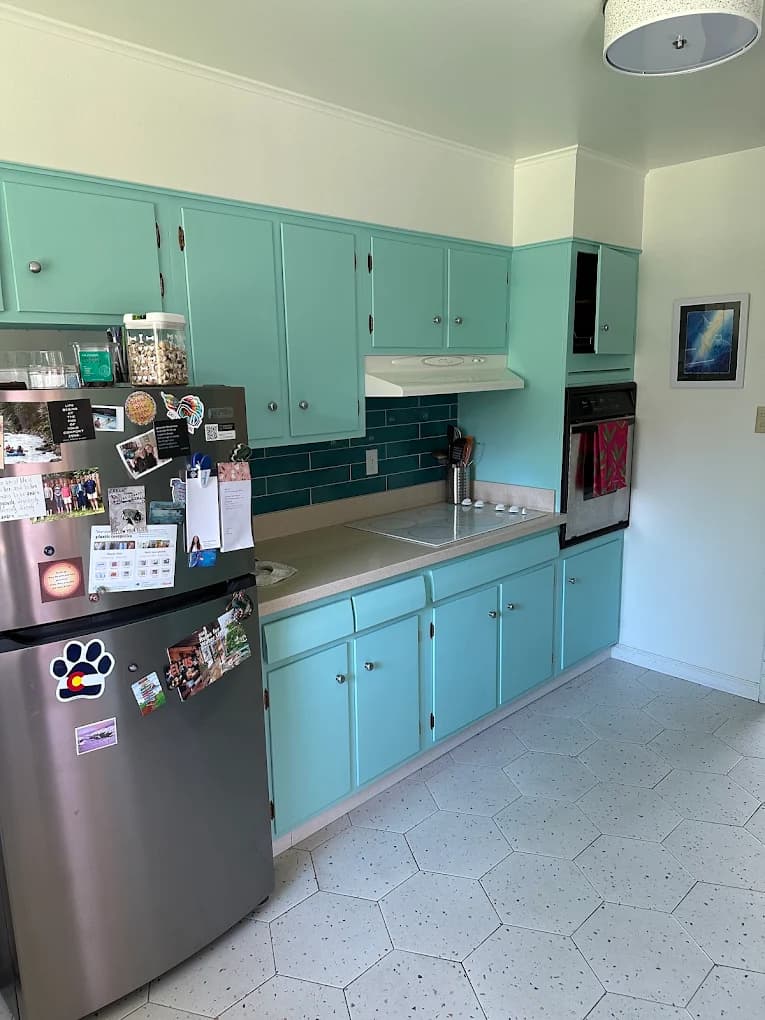 Mint green kitchen cabinets beside a stainless fridge