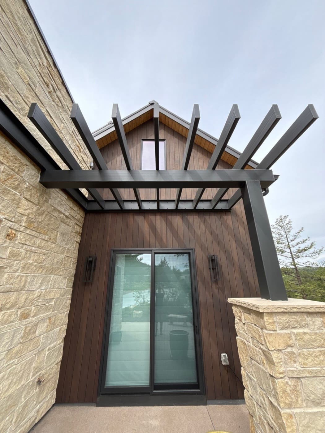 Stained vertical siding and a black steel pergola over a patio door
