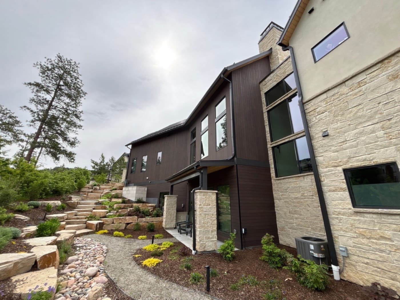 Mountain-modern home in stone and dark stained siding above a boulder staircase