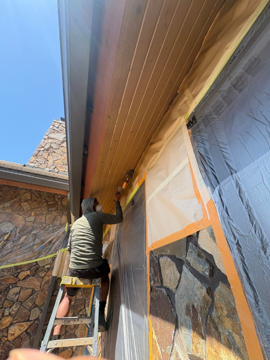 Painter on a ladder staining a soffit above masked stonework