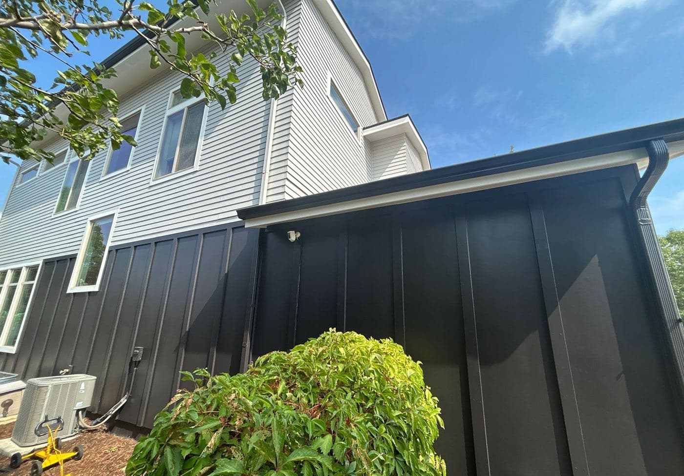 Black board-and-batten lower storey beneath pale gray lap siding