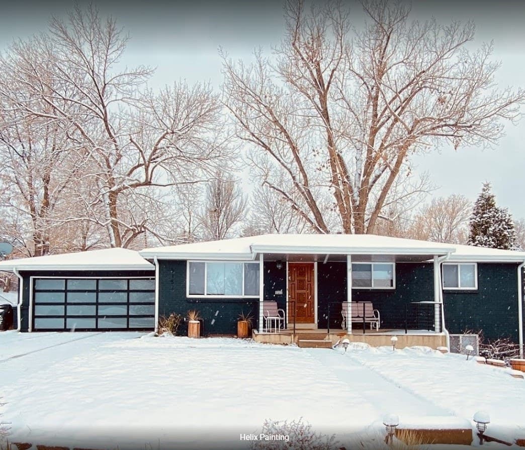 Ranch home with its brick painted deep green and white trim, under fresh snow