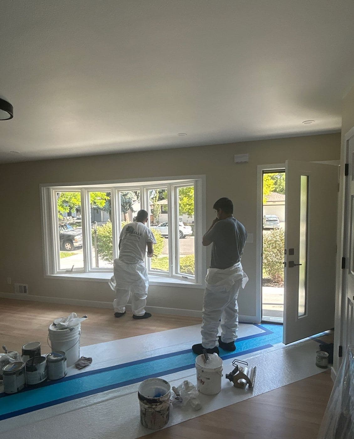 Two Helix painters cutting in around windows on a covered floor